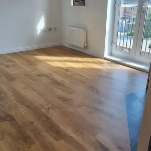 A spacious room featuring newly installed Karndean Van Gogh Auckland Oak flooring. The oak planks exhibit a rich, warm brown color with natural wood grain patterns that add texture and depth to the space. The room is well-lit, highlighting the elegant and realistic wood finish that seamlessly covers the floor, creating a sophisticated and inviting atmosphere.